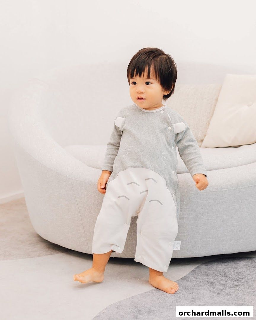 A young child in a cute Totoro-themed romper sits on a modern sofa.