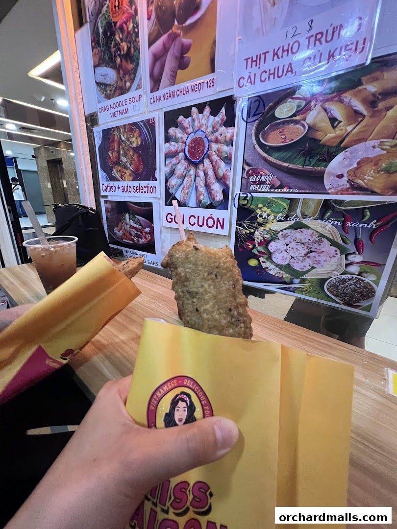 A hand holds a fried item in a yellow wrapper from Miss Saigon Singapore.