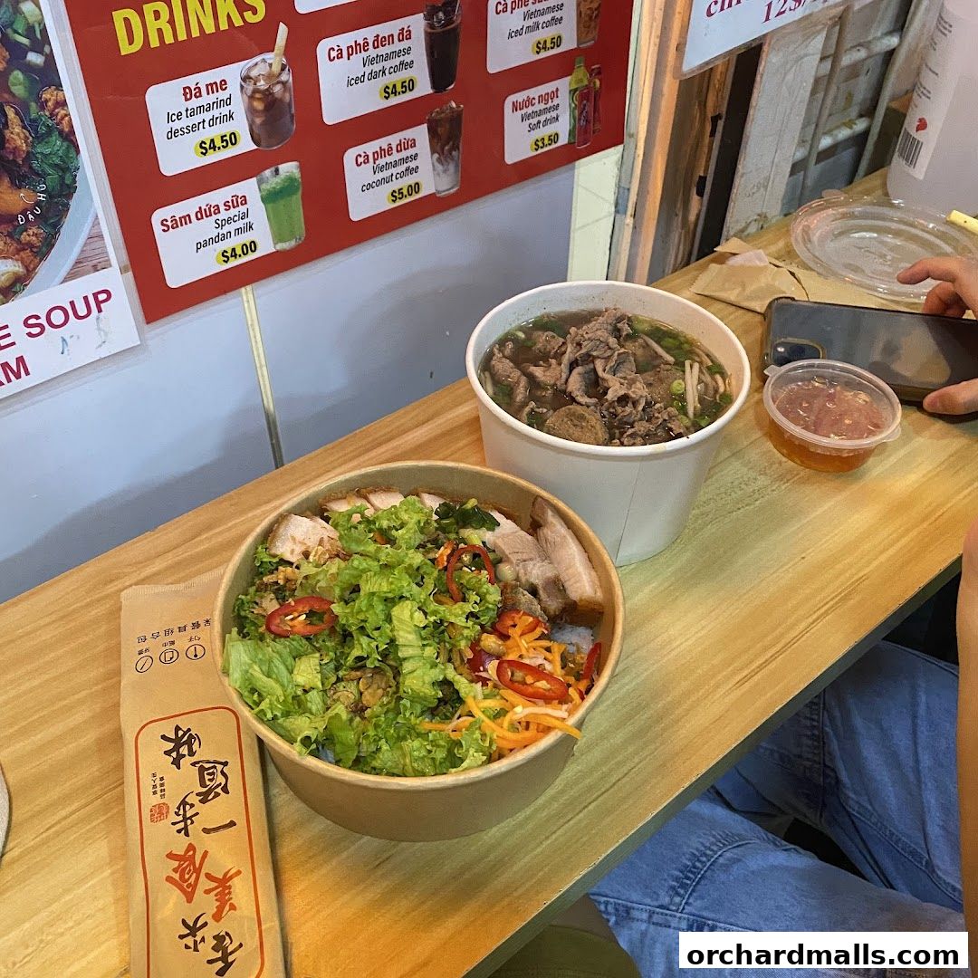 A table with Vietnamese food and drinks, including pho and a salad bowl.