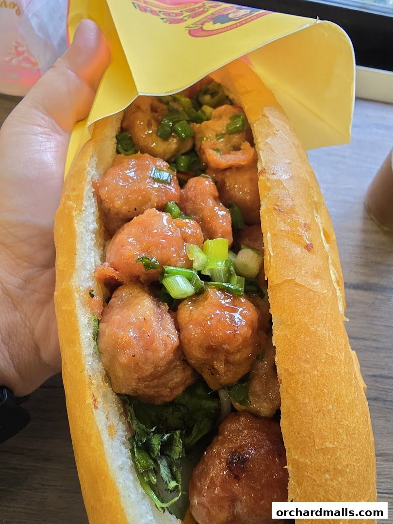 A hand holds a delicious Vietnamese meatball banh mi sandwich.