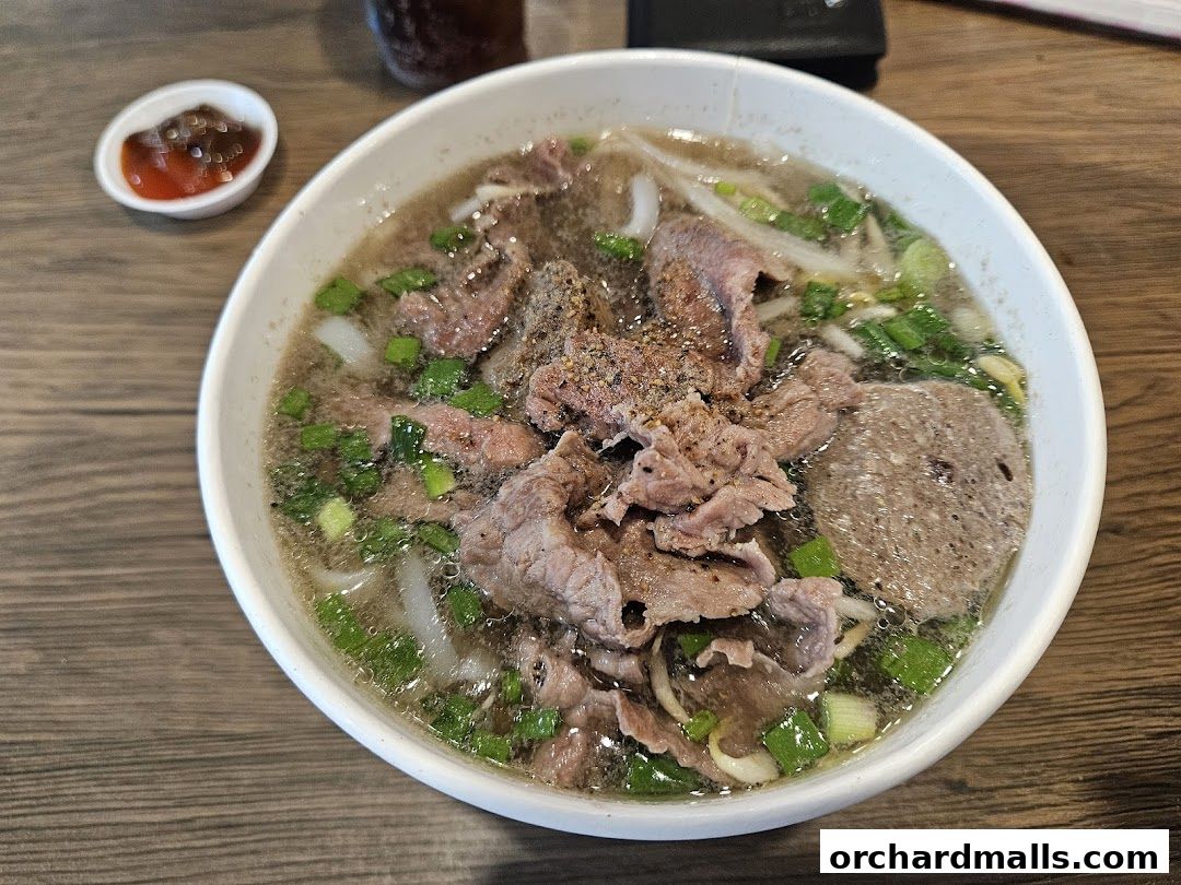A steaming bowl of beef pho with sliced beef, noodles, and green onions.