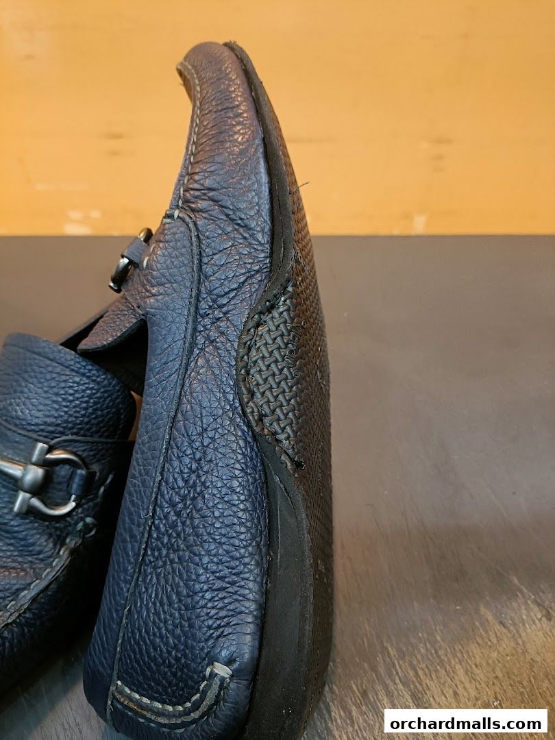 Close-up of a worn navy blue leather loafer with a silver buckle.