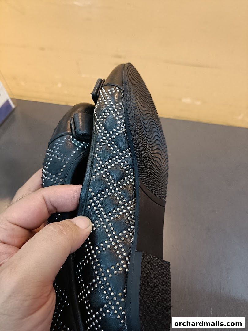 A hand holds a black studded flat shoe, showcasing its detailed design and sole.