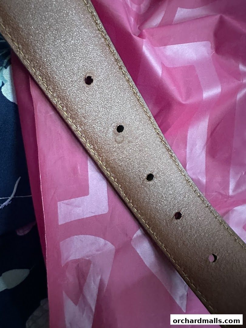 A close-up of a brown leather belt with multiple holes against a pink background.