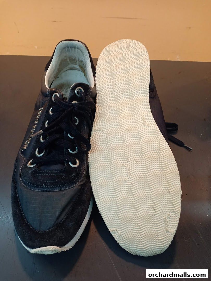A pair of black Louis Vuitton sneakers, one showing the sole, on a dark surface.