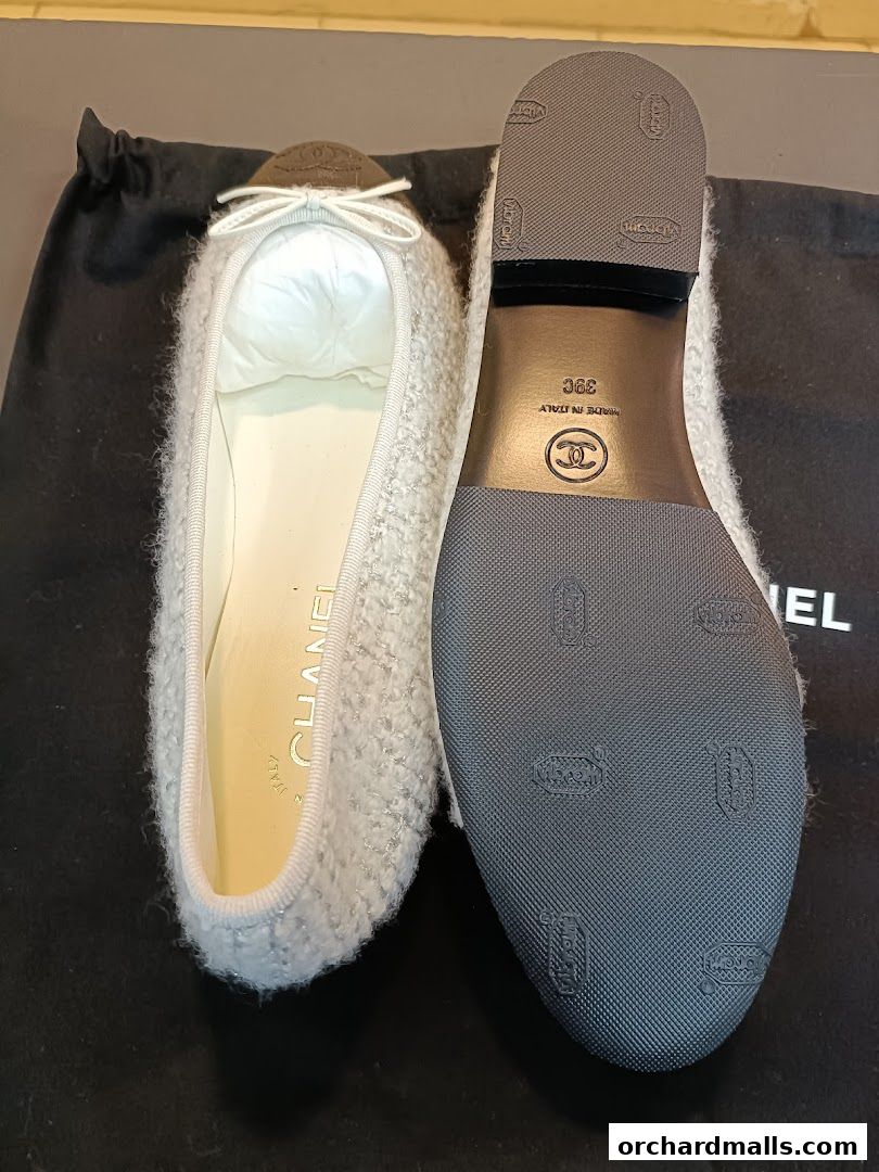 A pair of white Chanel ballet flats with a textured exterior and a black sole.