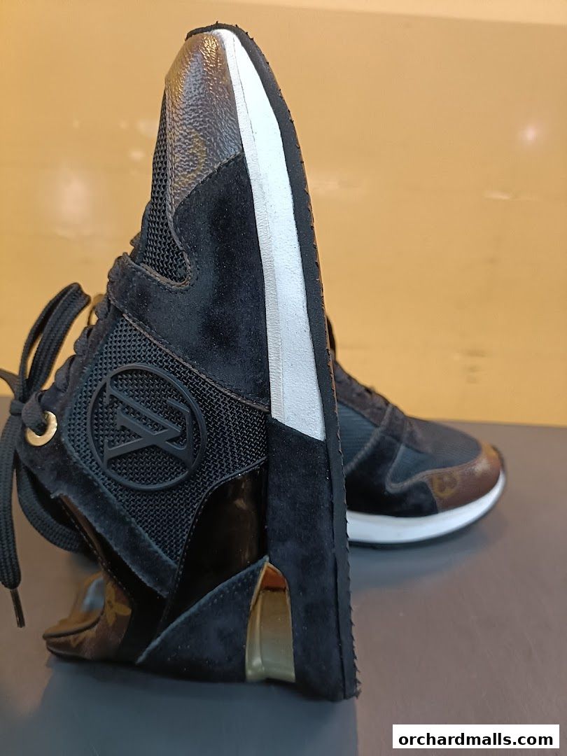 Close-up of a stylish black sneaker with gold accents and signature monogram pattern.