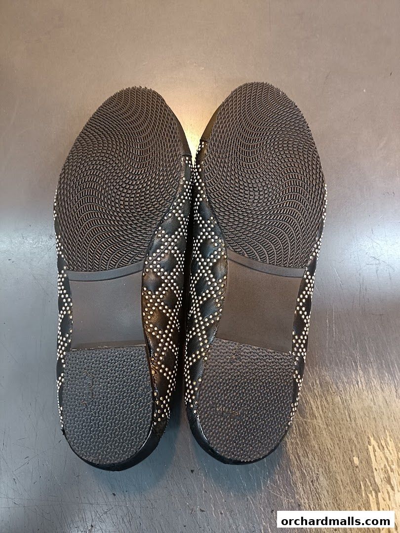Close-up view of the soles of two black studded ballet flats.