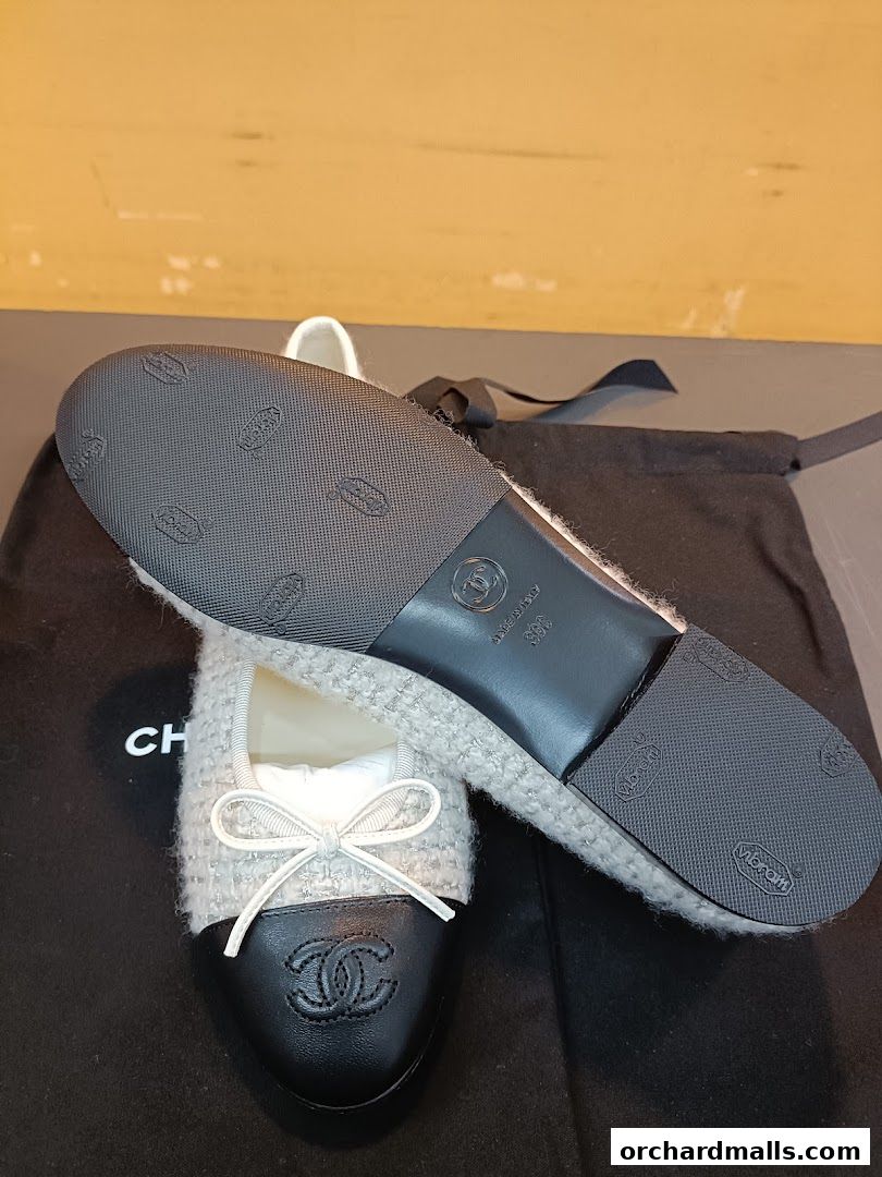 Chanel ballet flats with a tweed upper and black cap toe, displayed on a dust bag.