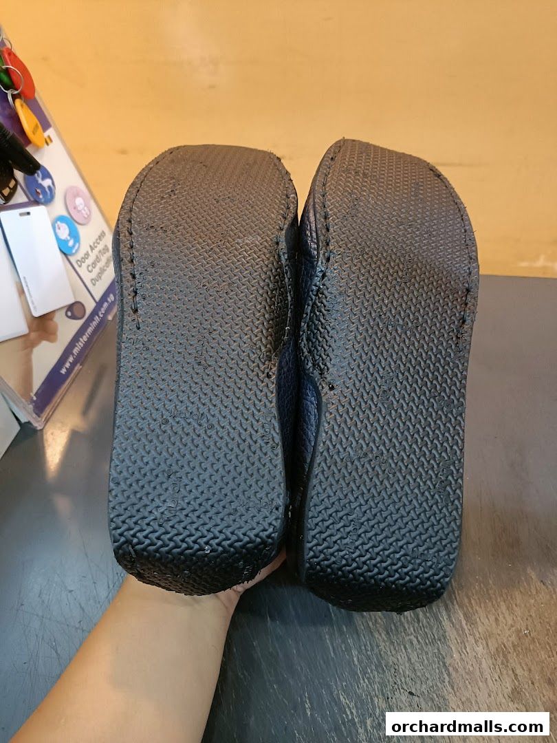 A pair of dark blue shoes, viewed from the soles, with a display of keychains and cards in the background.