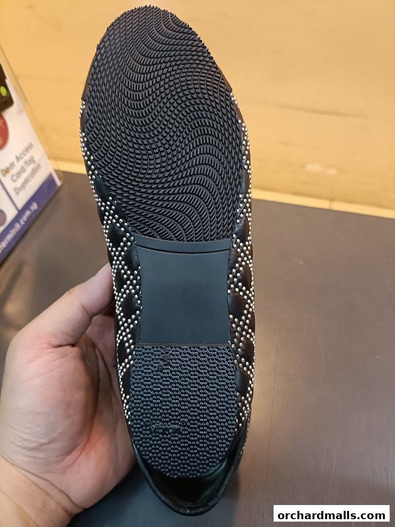 A hand holds the sole of a black quilted shoe with silver stud detailing.