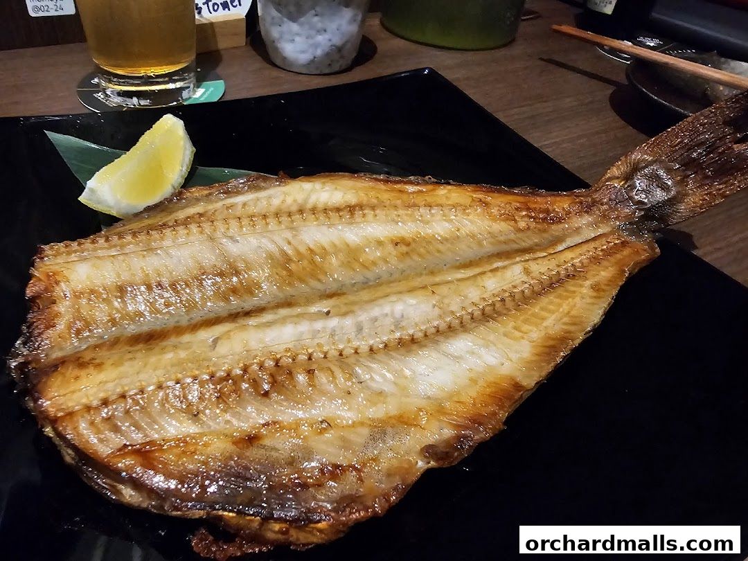 A perfectly grilled fish served with a lemon wedge on a black plate.