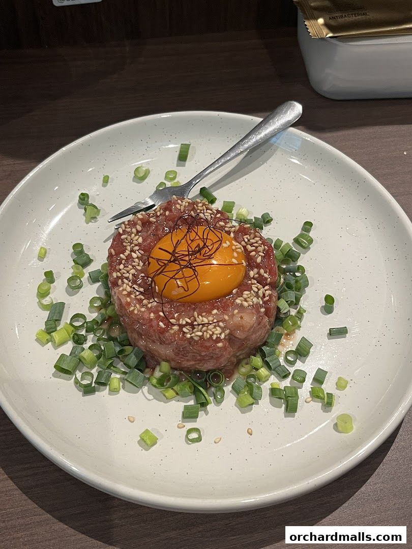A plate of Japanese Obanzai izakaya dish with raw beef, egg yolk, and scallions.