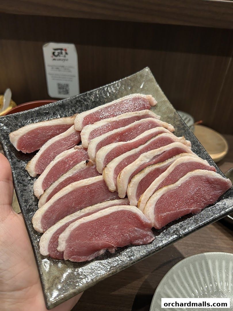 A plate of thinly sliced raw duck breast with skin, seasoned and ready to be cooked.