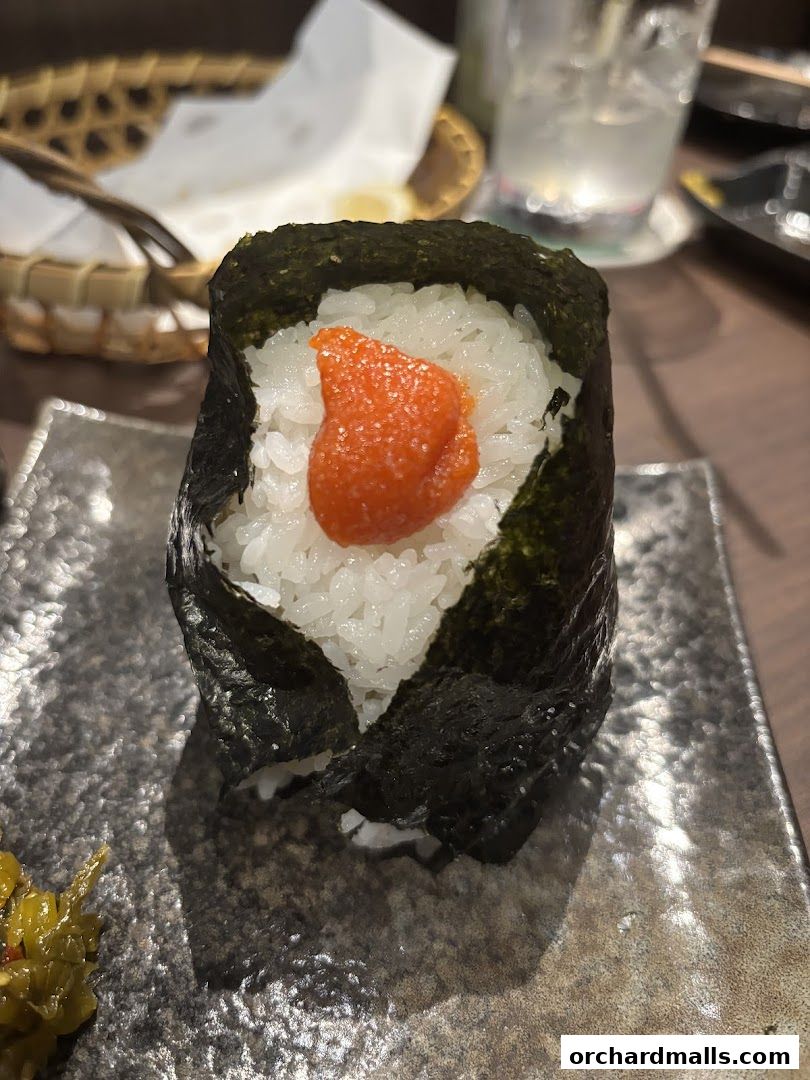 A close-up of a Japanese rice ball wrapped in nori seaweed with a dollop of orange roe.