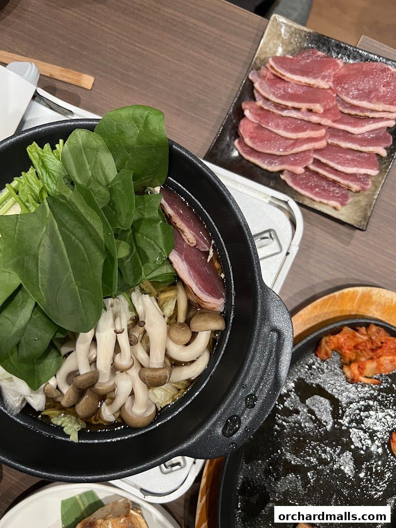 A close-up of a Japanese hot pot with vegetables and mushrooms, alongside sliced meat and kimchi.