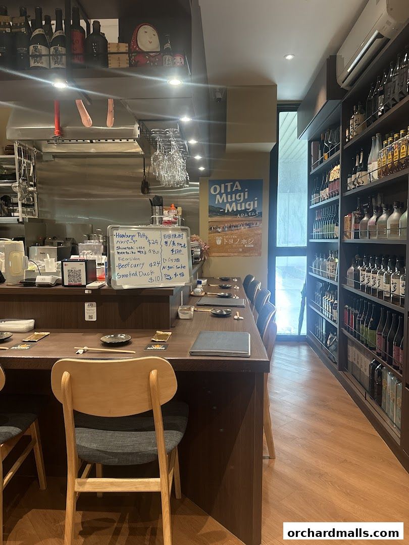 Interior of a Japanese izakaya with a counter, menu board, and shelves of sake bottles.