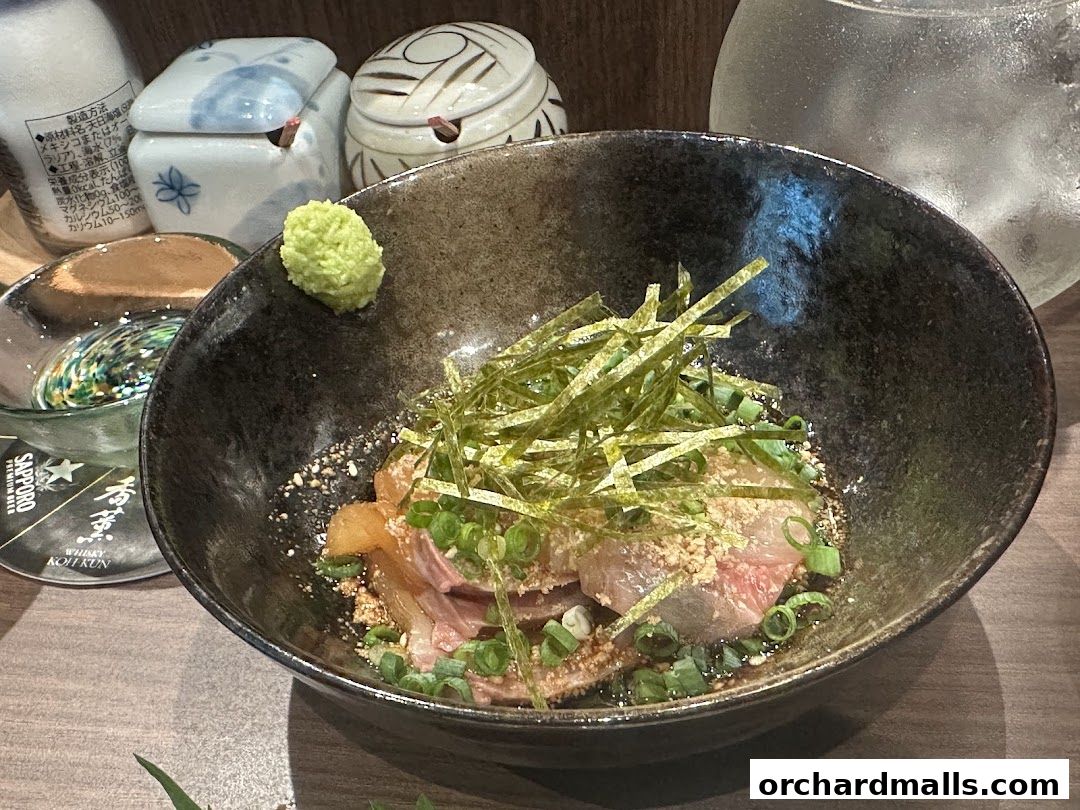 A close-up of a Japanese dish with thinly sliced fish, seaweed, and green onions in a dark bowl.