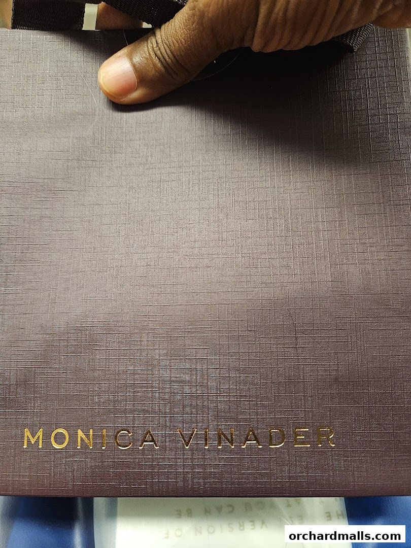 A hand holds a textured shopping bag with the Monica Vinader logo.