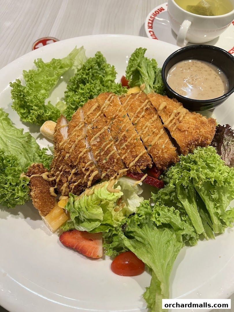 A delicious salad with crispy chicken, fresh lettuce, strawberries, and a side of dressing.