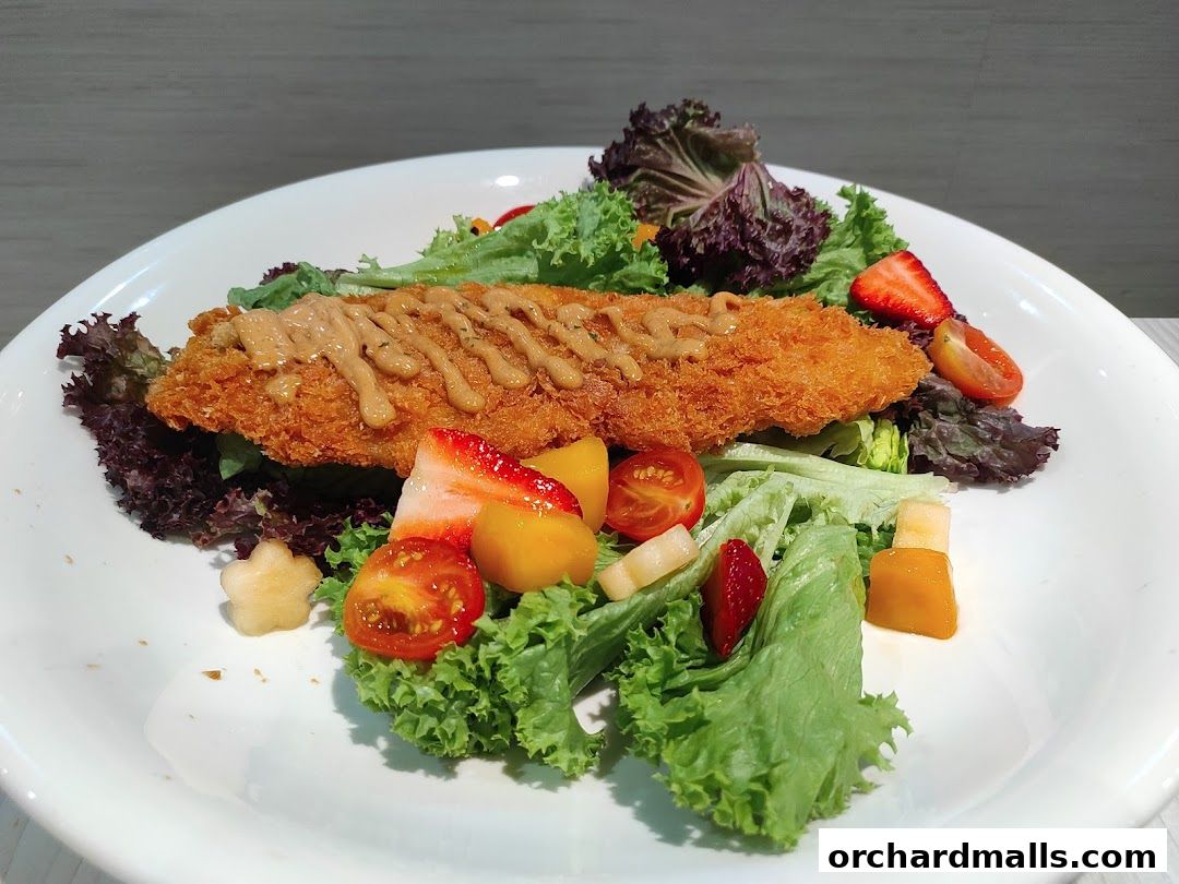 A close-up of a crispy fried fish fillet served on a bed of fresh salad with fruits.