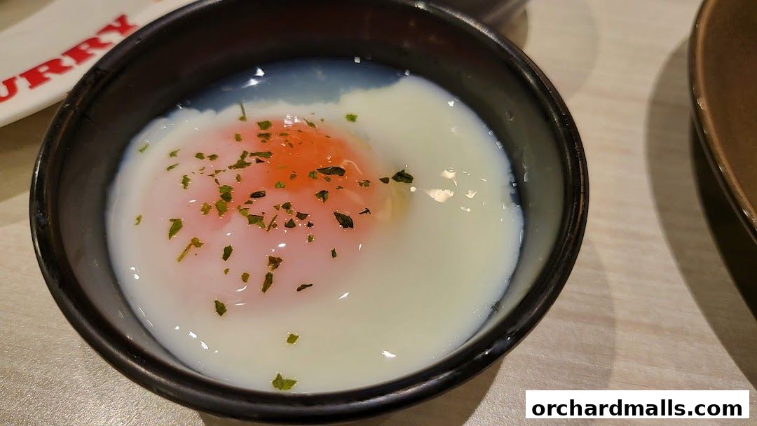 A close-up of a soft-boiled egg in a black bowl, garnished with herbs.
