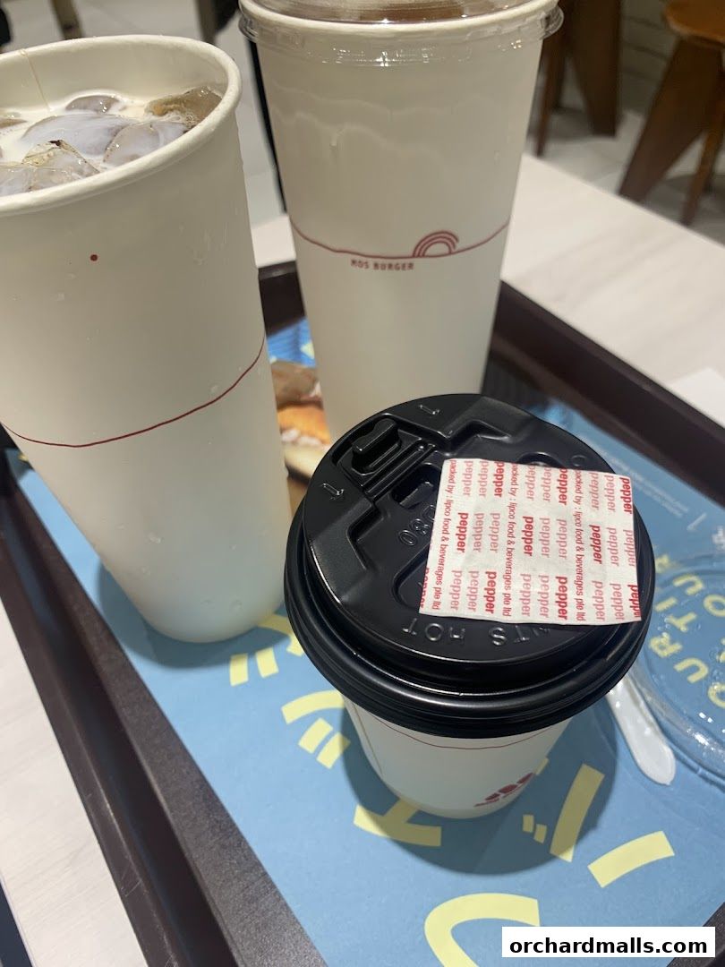 Three cups of drinks from MOS Burger, one with a black lid sealed with pepper packets.