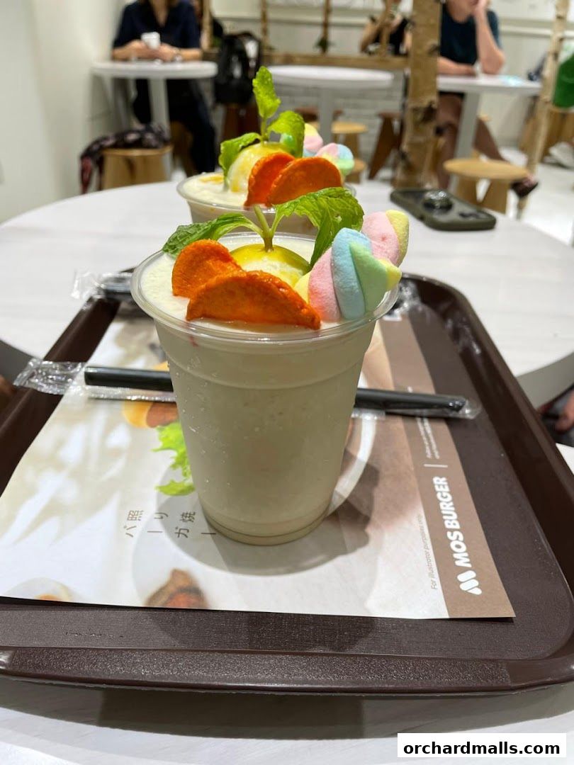 A close-up of a creamy milkshake topped with marshmallows, fruit slices, and mint leaves.