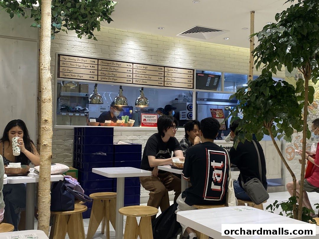 Diners seated at tables inside a MOS Burger restaurant, with a menu board visible above the counter.