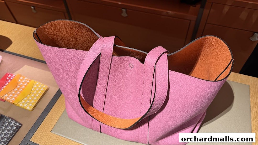 A pink leather tote bag with orange lining is displayed on a counter.