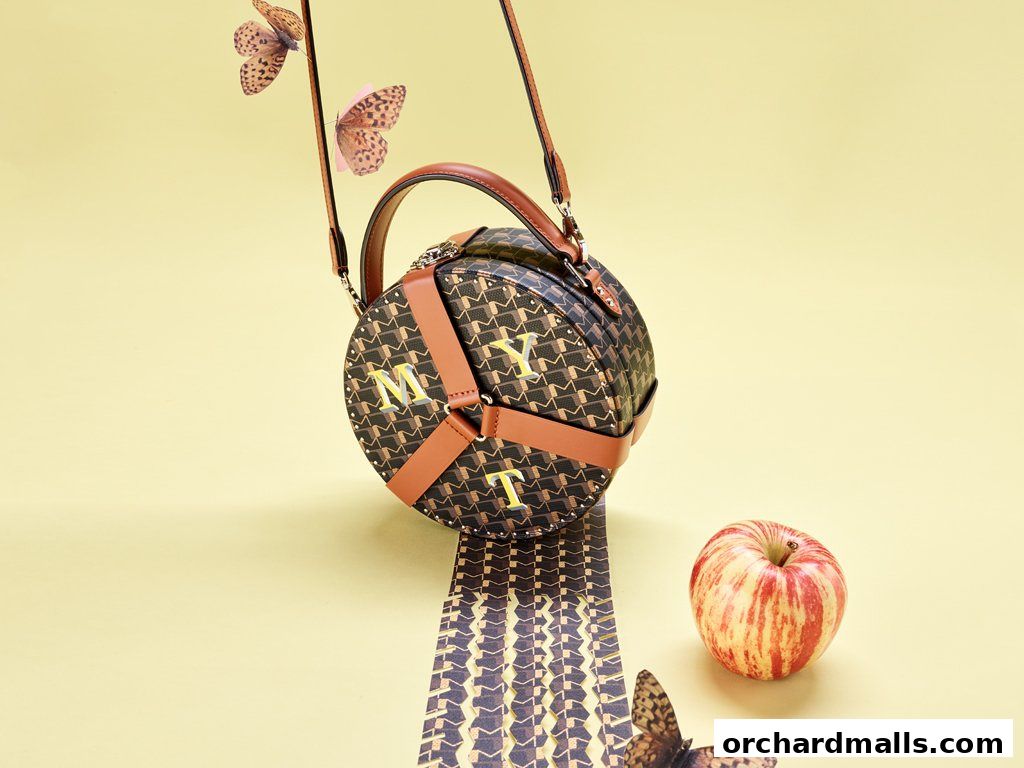 A circular MOYNAT handbag with monogram pattern and leather accents, styled with butterflies and an apple.