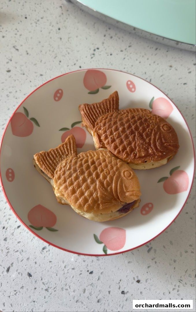 Two fish-shaped Japanese pancakes filled with purple sweet potato paste on a peach-patterned plate.