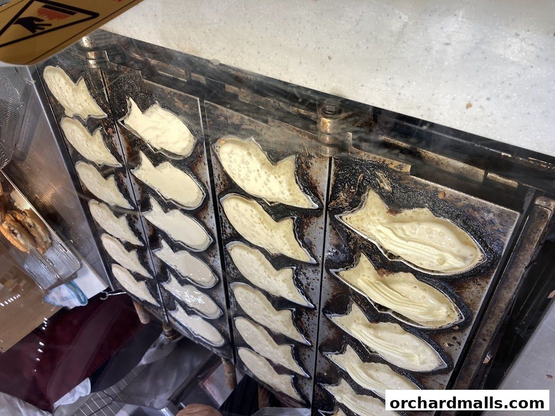 A close-up of a taiyaki maker with batter being poured into fish-shaped molds.