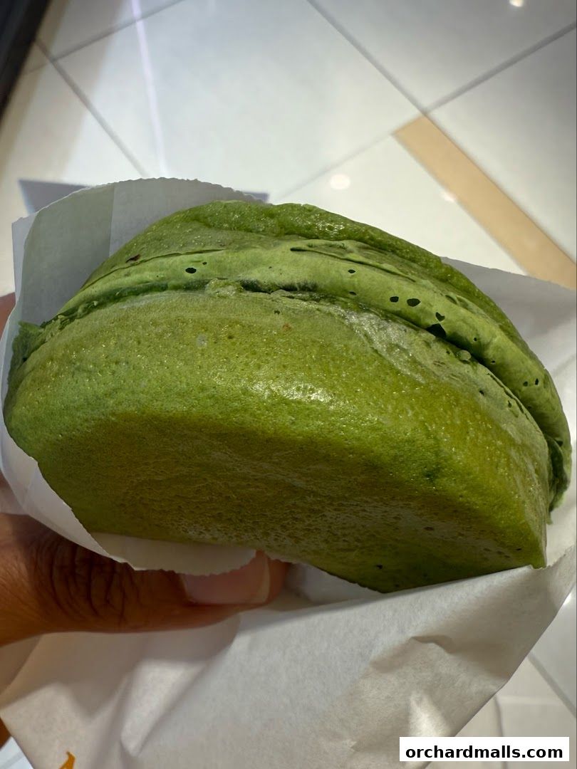 A hand holds a green matcha taiyaki pancake wrapped in white paper.