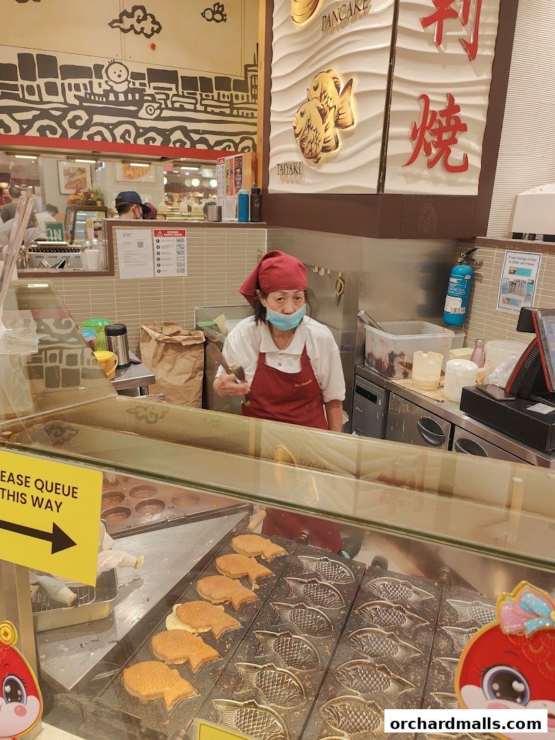 A vendor prepares Japanese fish-shaped pancakes at a counter with fresh batter and molds.