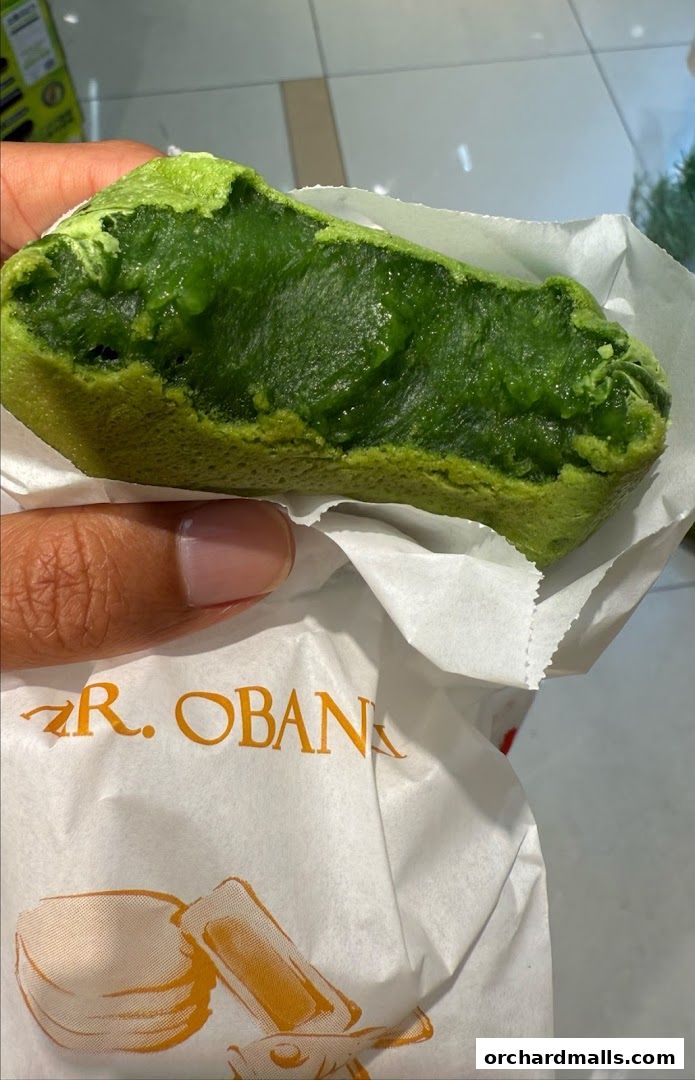A hand holds a green matcha taiyaki pancake filled with cream.