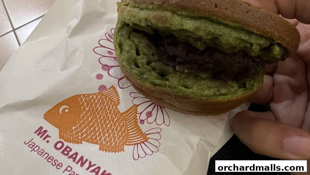 A close-up of a green matcha taiyaki pancake filled with red bean paste.