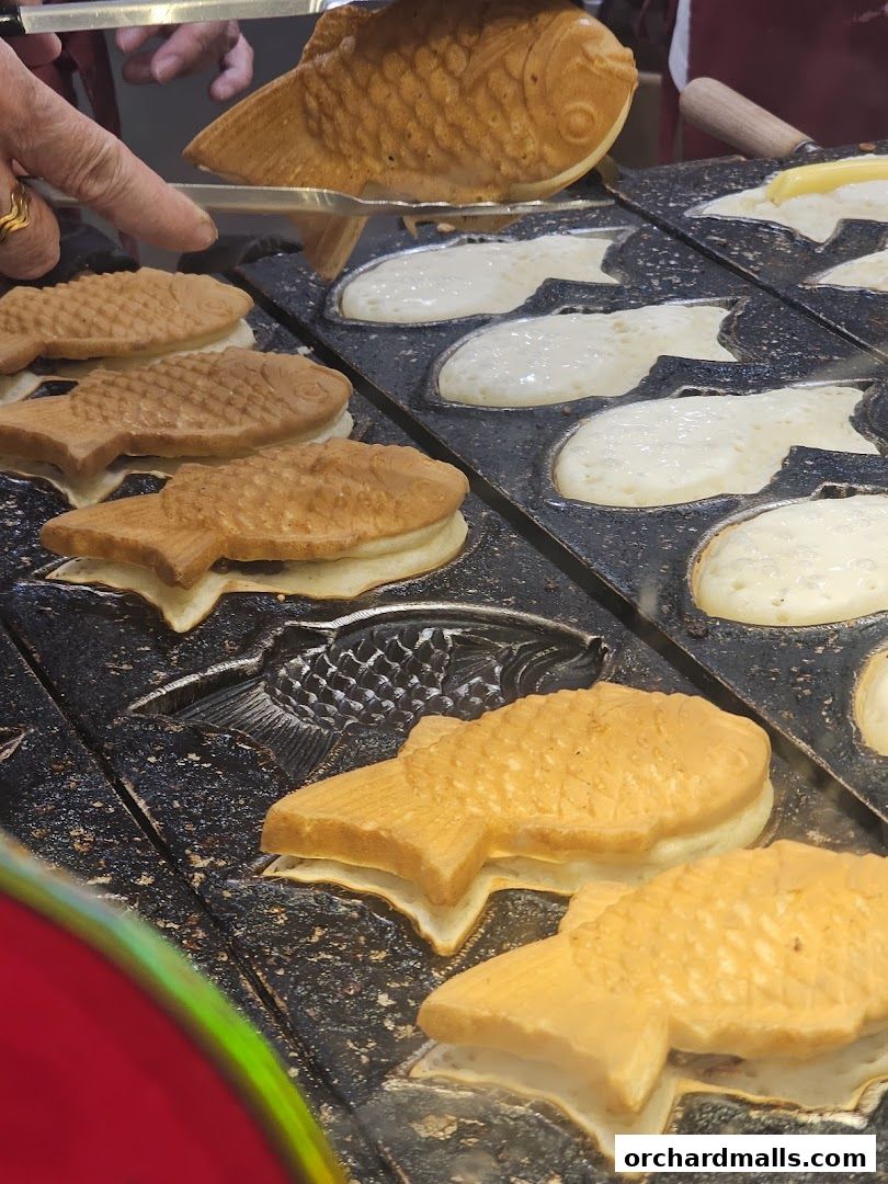 Freshly made fish-shaped Japanese pancakes being cooked on a griddle.