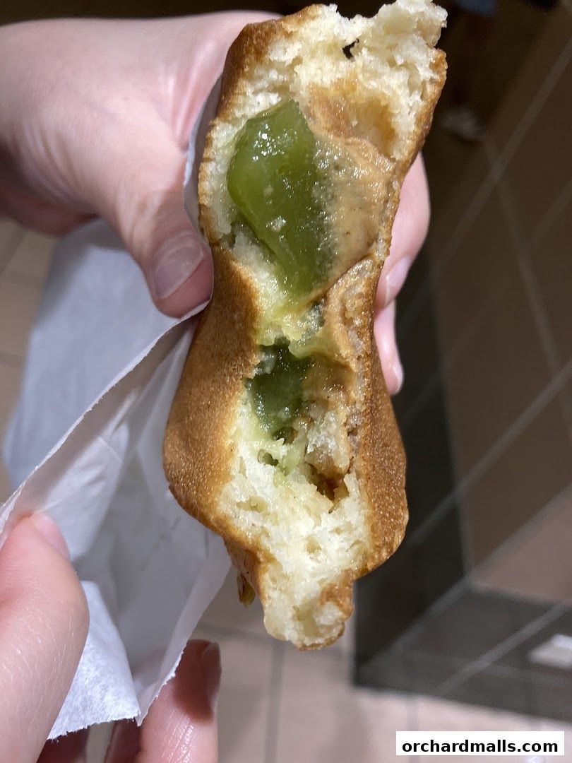 A close-up of a person holding a half-eaten Japanese pancake filled with green jelly and cream.