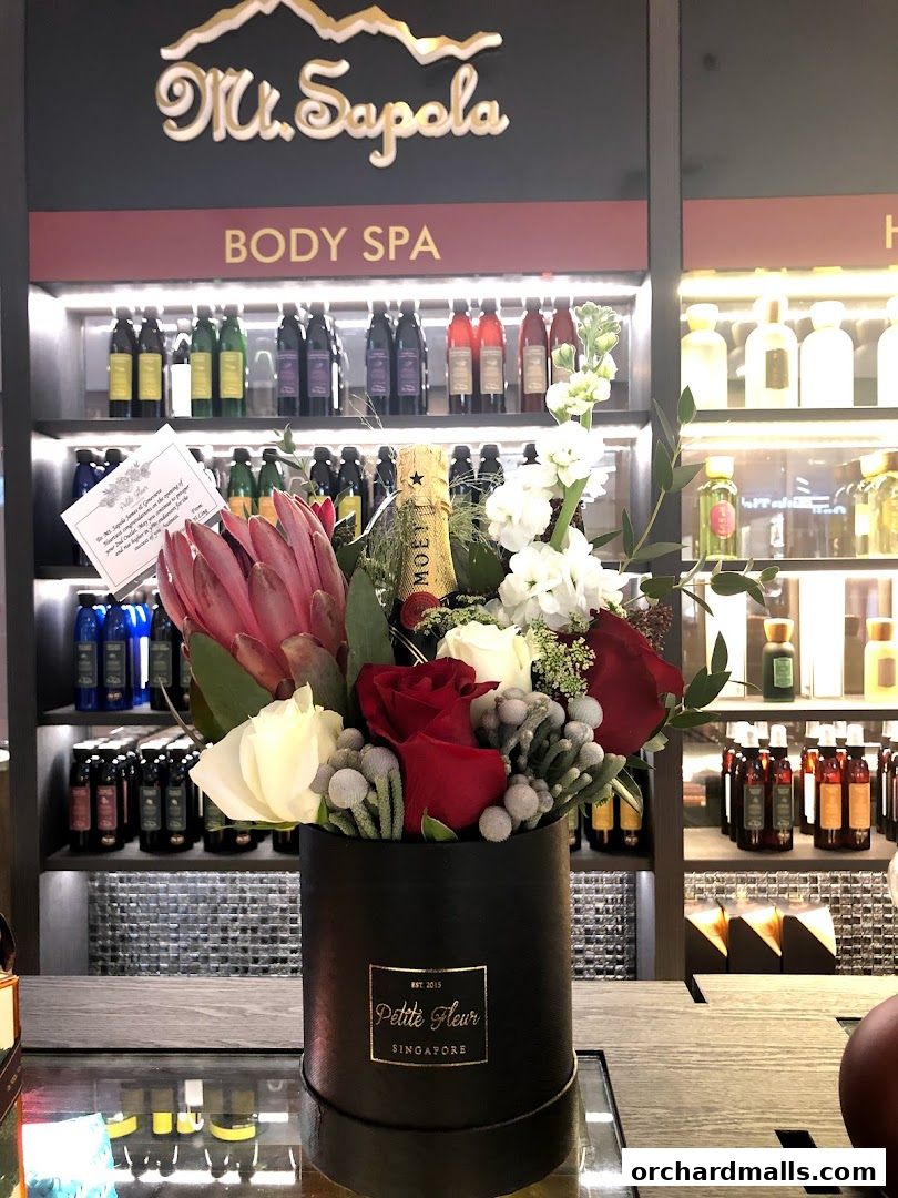 A floral arrangement with a bottle of champagne in front of a display of body spa products.