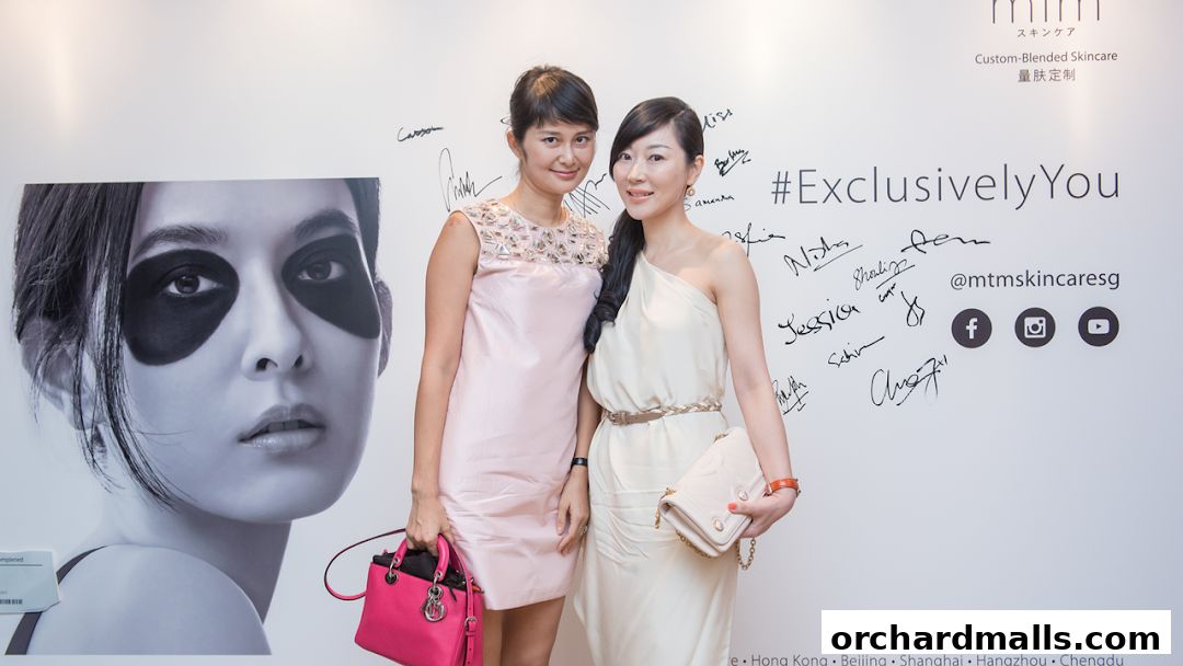 Two women pose in front of a wall with a large skincare advertisement and signatures.