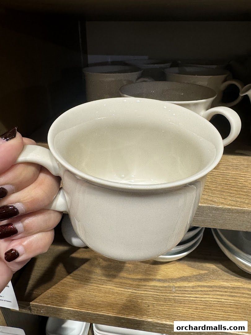 A hand holding a light-colored ceramic mug with a wide opening and a handle.