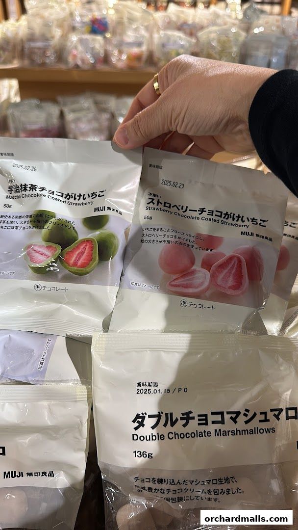 A hand holds bags of MUJI chocolate-coated strawberries and marshmallows.