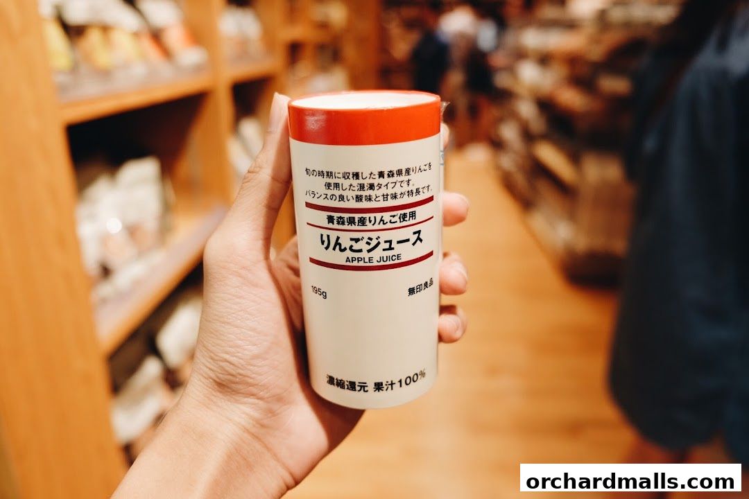 A hand holds a can of MUJI apple juice with Japanese text and English label.