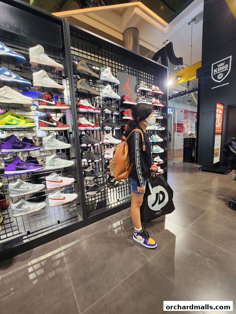 A young person wearing a mask stands in a shoe store, browsing a wide selection of sneakers.