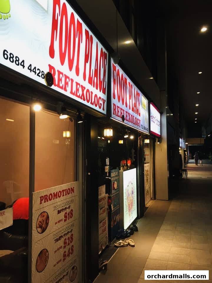 Exterior of 'My Foot Place Reflexology' shop with illuminated signs and promotional posters.