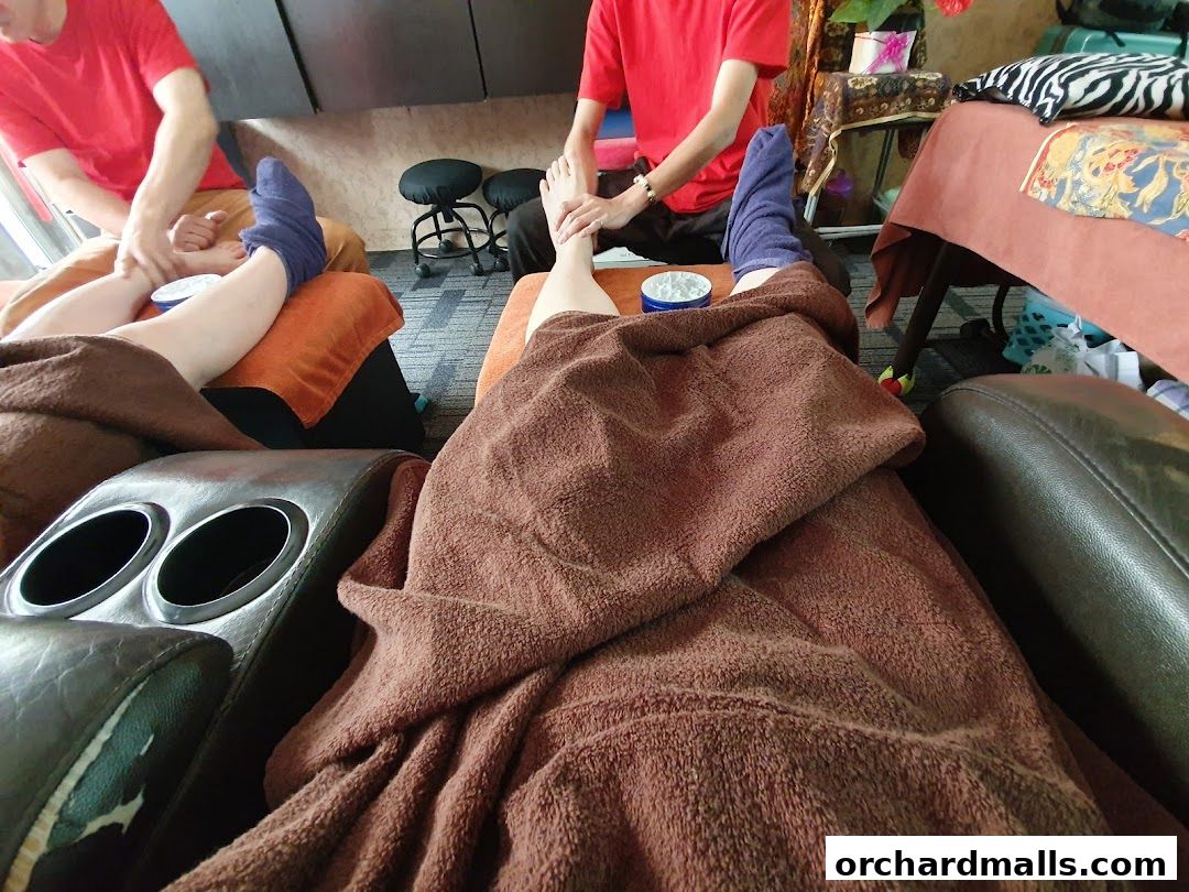 Two people receiving reflexology foot massages in comfortable chairs.