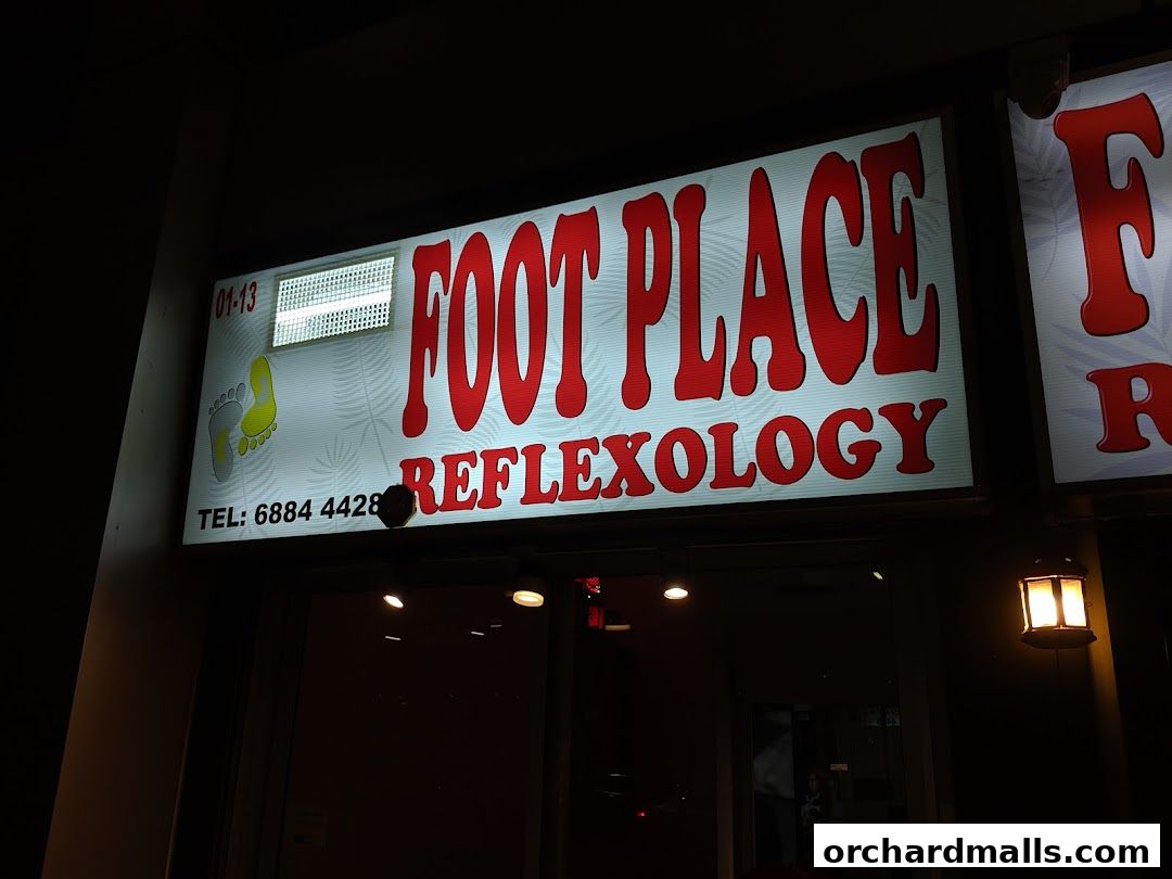 A brightly lit sign for 'My Foot Place Reflexology' at night.