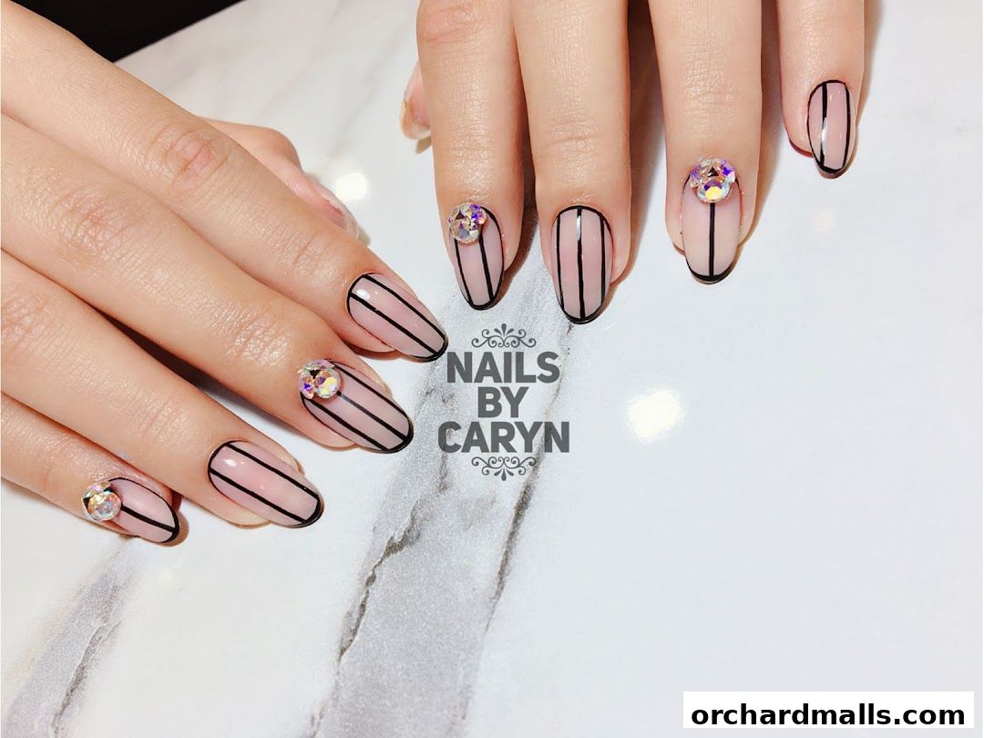 Close-up of hands with stylish nude nails featuring black stripes and rhinestones.