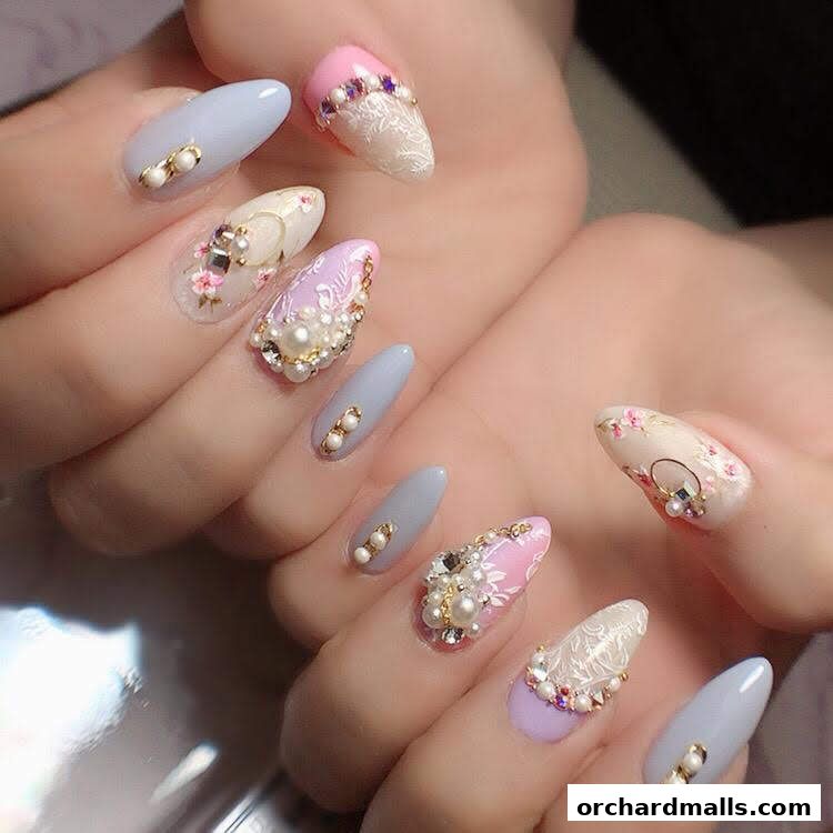 Close-up of hands with intricately designed, embellished almond-shaped nails.